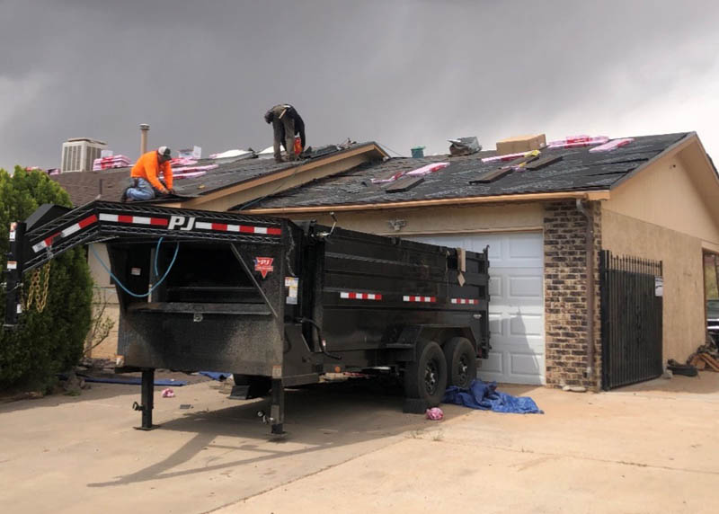 Workers on the roof of a house tear off shingles. 
