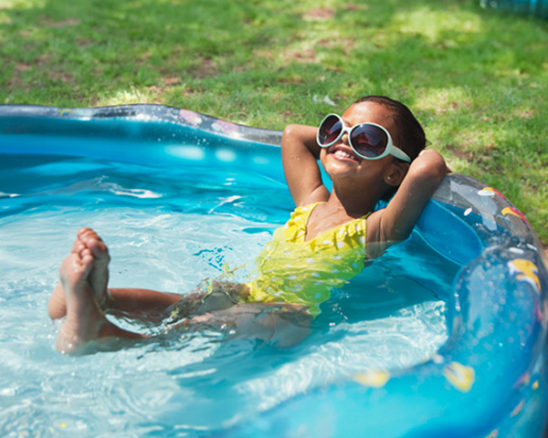 African American girl lounging in a kiddie pool with sunglasses on her face.