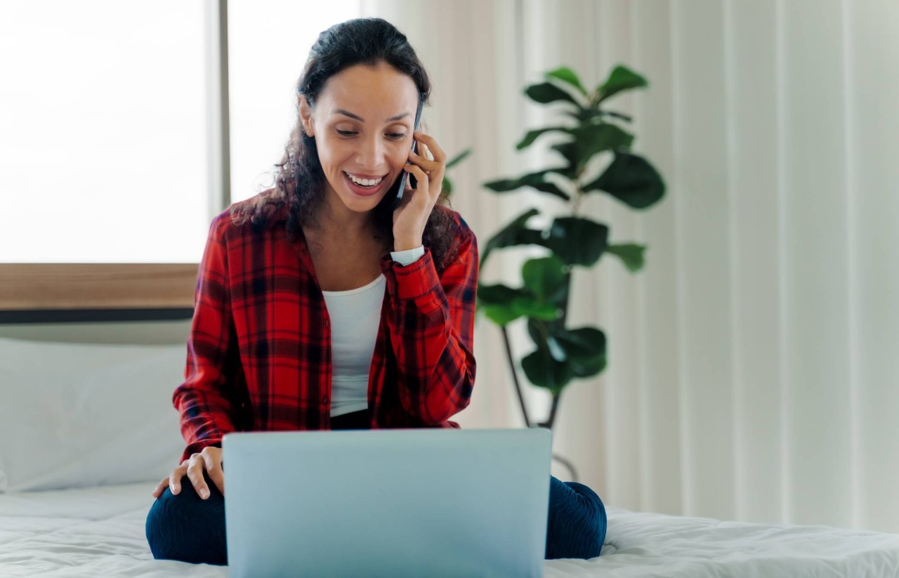 Mujer sentada detrás de una computadora portátil, mientras habla por teléfono
