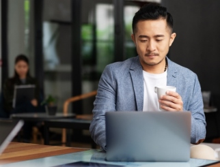hombre frente a la computadora con un café en la mano
