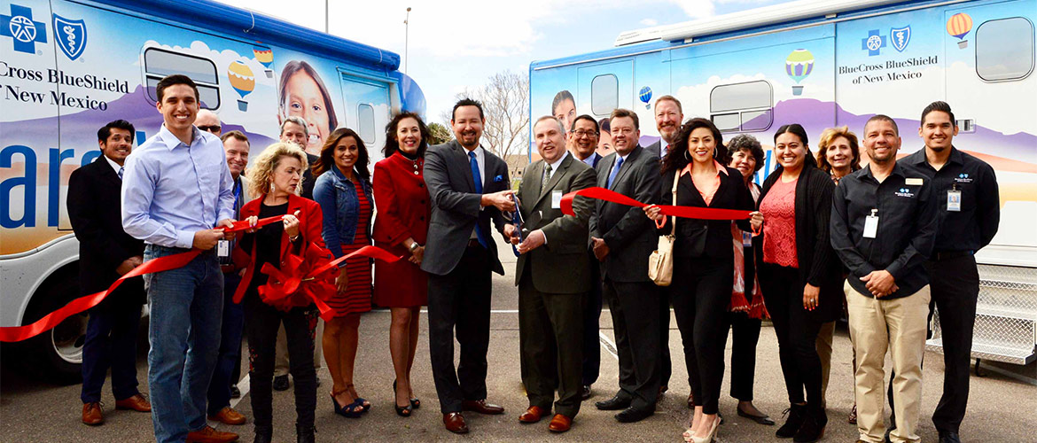 A group of men and women cut a red ribbon outdoors surrounded by Care Vans