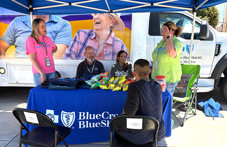 Five people gather outside around a blue table in front of a large medical van
