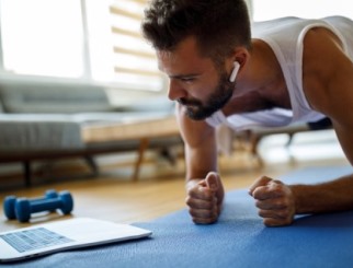 oung man doing a plank exercise on his living room rug, watching an exercise video or live feed on his laptop.