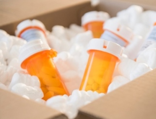 Cardboard box filled with six orange prescription bottles set in packing peanuts