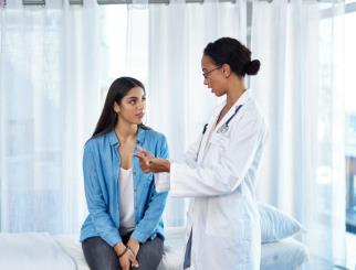 Young woman sitting on an exam table, speaking with her doctor.