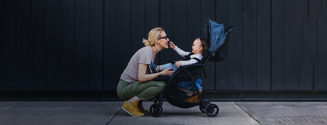 Mother crouching in front of her child in a stroller as the child reaches out for her.