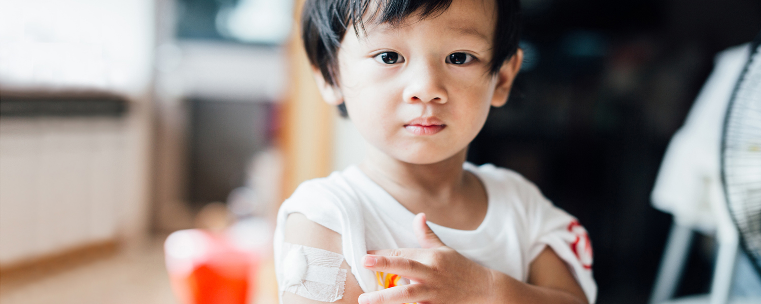 A young boy looks forward, displaying a bandage on his arm