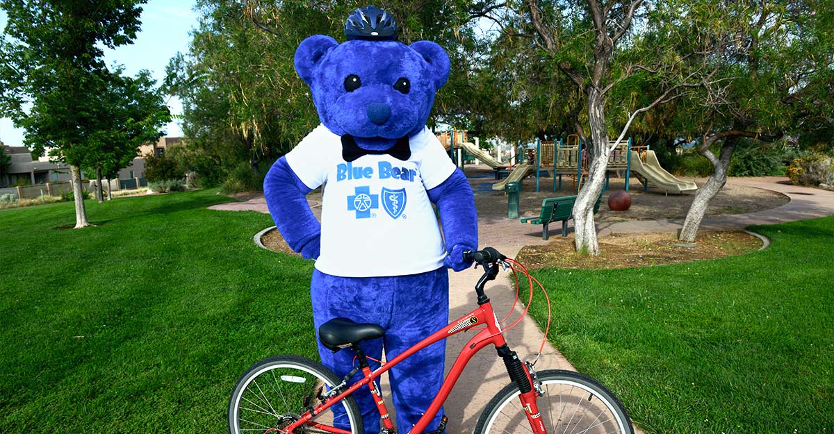 Blue Cross and Blue Shield of New Mexico mascot posing with children's bicycle