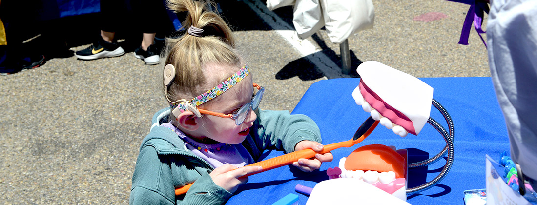 A young girl with glasses and a hearing aid examines a dental display.