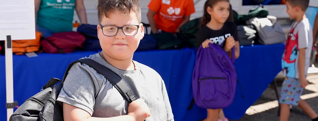 Young boy poses with backpack at school supply giveaway
