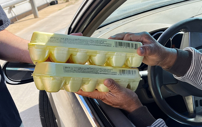 Two cartons of eggs being handed to the driver of a car at a drive-by food drive