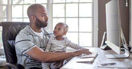 Man on computer holding a baby