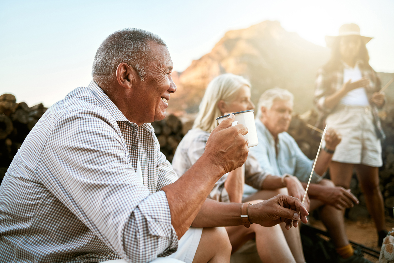 Relaxed senior camping with friends, taking a break and drinking a cup of coffee. 